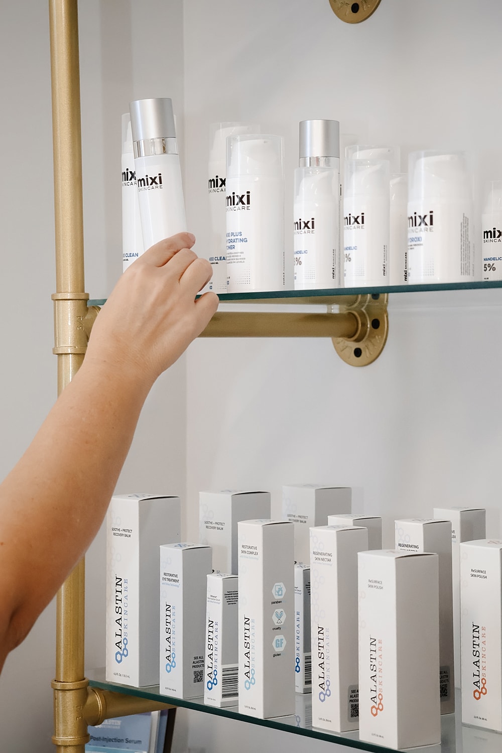 Hand reaching for skincare products on a shelf.